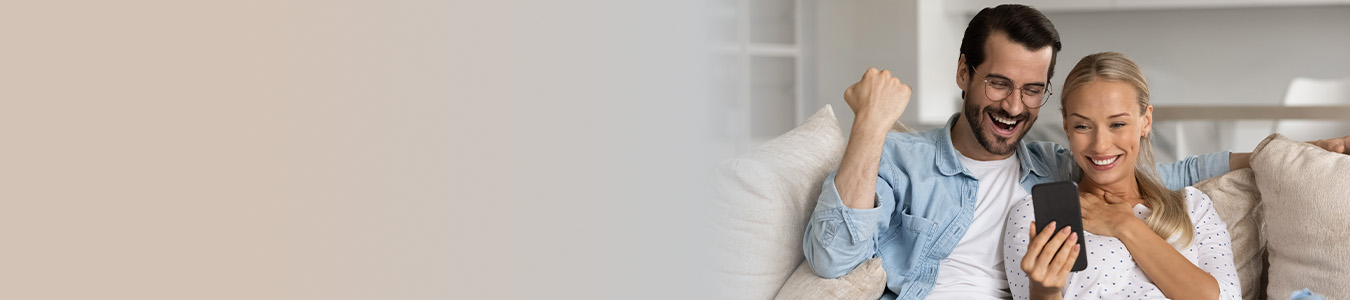 a happy couple sitting on their couch with a smartphone