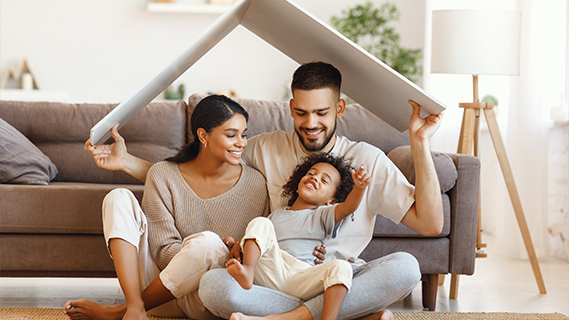 a family of three sitting and smiling on the floor in front of their  couch