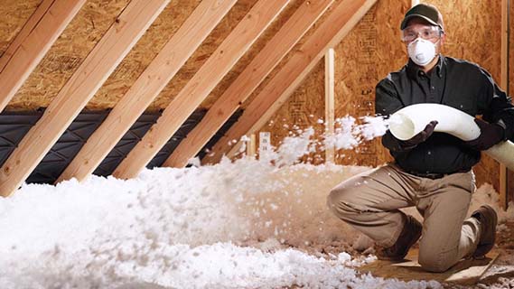 man wearing proper PPE blowing ceiling insulation into attic of home