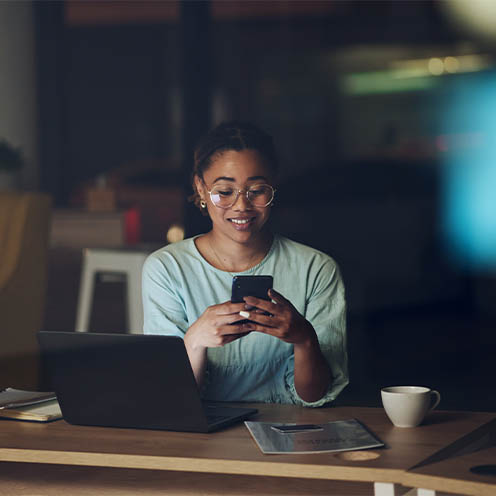 a woman sitting at her table using her laptop and phone