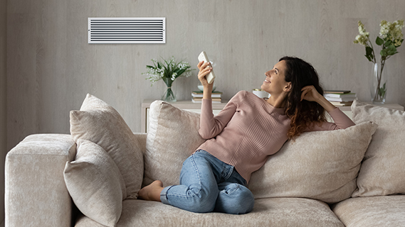 a woman sitting cross-legged on a beige couch holding an a/c remote control