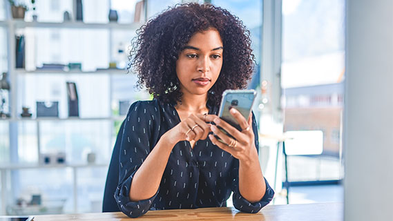 a woman sitting at a wooden desk using her smartphone