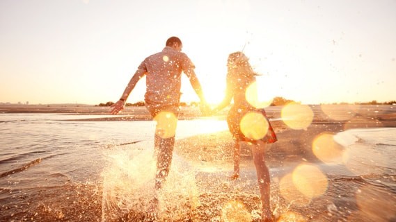 Man and woman running through the water on the beach
