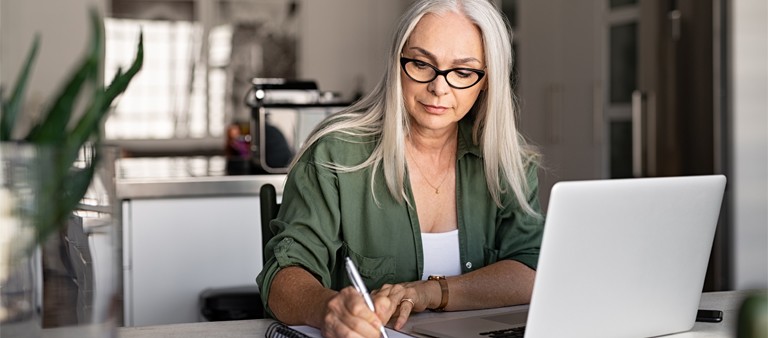 woman working at a desk in her kitchen with a notepad and computer