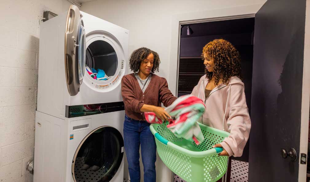 Two African American women putting clothes into a washer