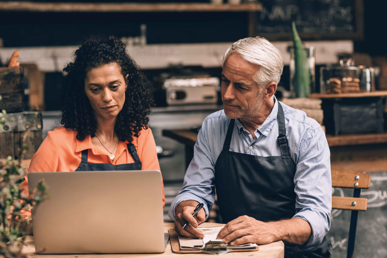 Two middled-aged business owners looking at a computer while sitting at a coffee shop