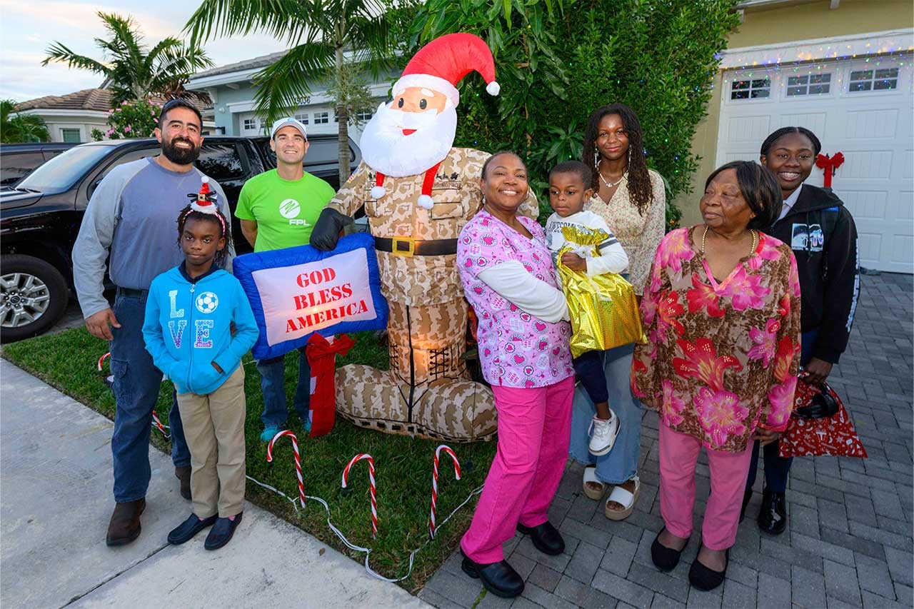 Holiday hero lighting - veteran in front of home with Santa inflatable and family