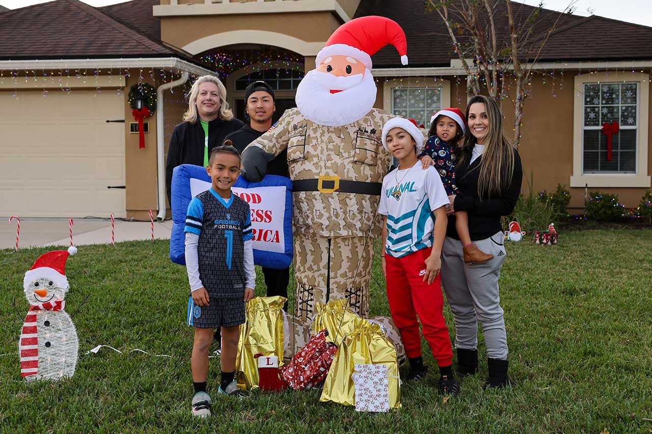 Holiday hero lighting - veteran in front of home with Santa inflatable and family
