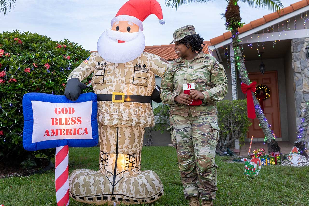 Holiday hero lighting - veteran in front of home with Santa inflatable