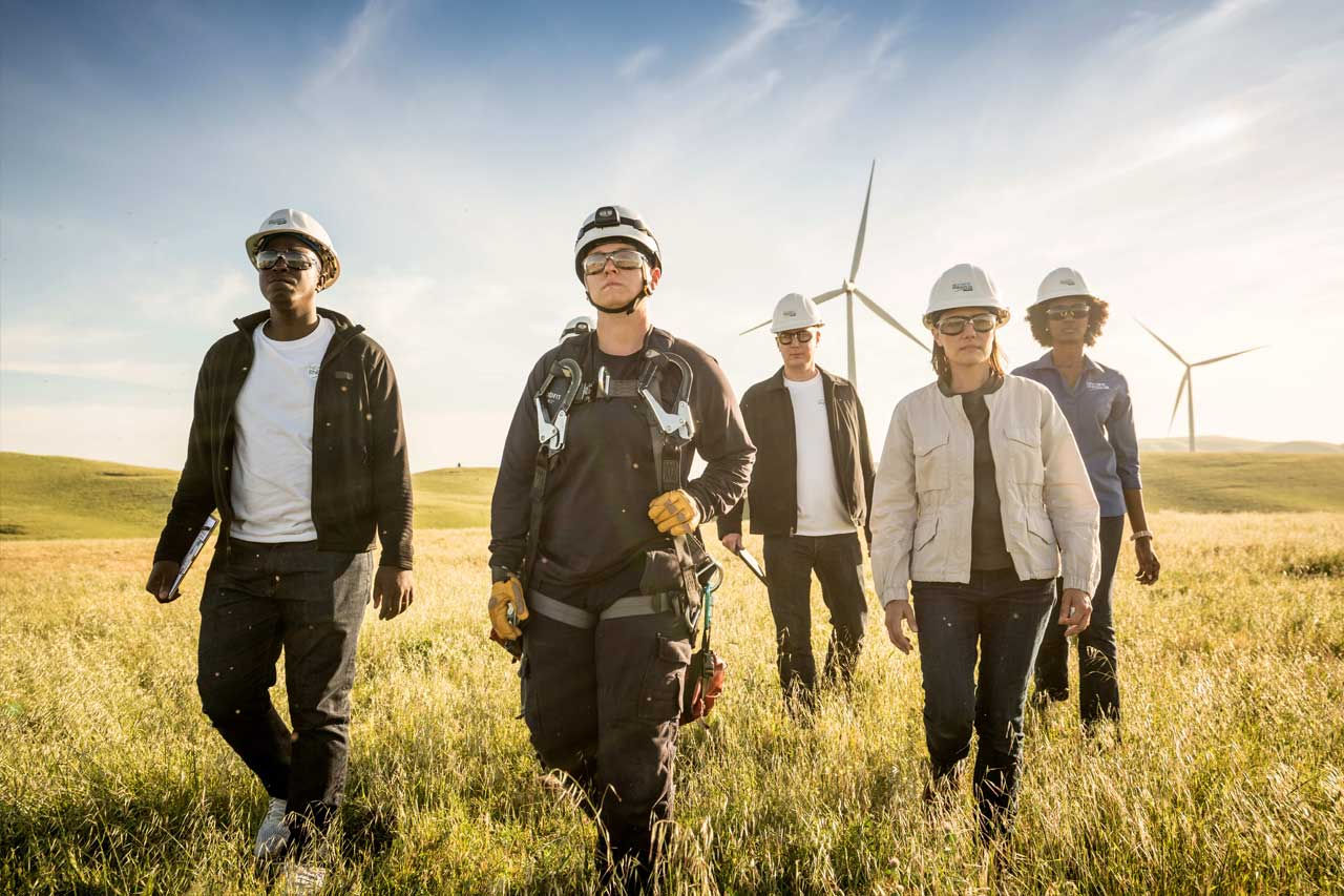 NEE employees walking with white helmets with a field of wind turbines behind them