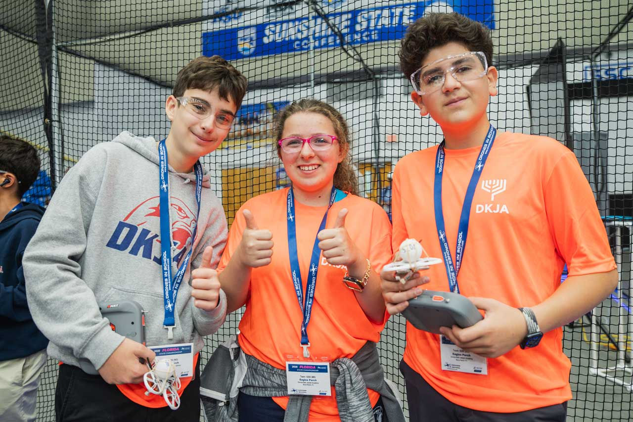 Two boys and a girl giving thumbs up and holding drone remotes