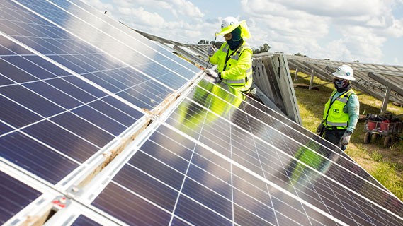 two fpl workers installing solar panels in an open field