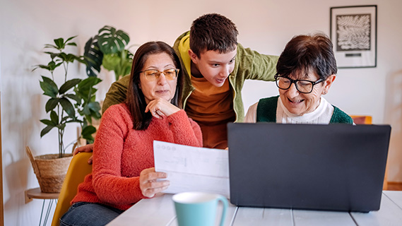 Mom, kid and grandma looking at a laptop and a piece of paper