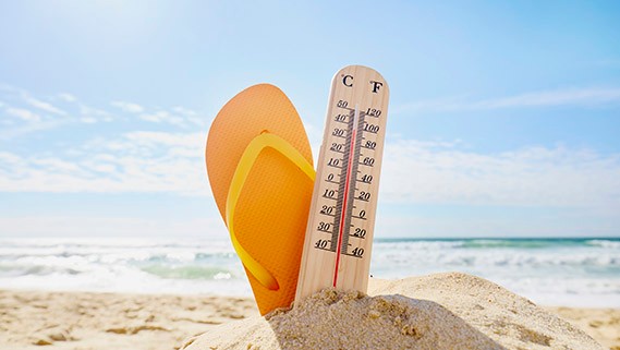 sandcastle with thermometer and flip-flop on the beach against sea, sun and blue sky