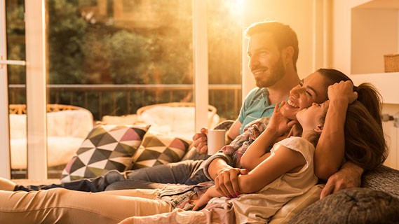 a family of three sitting on a couch in a warmly sun-lit living room
