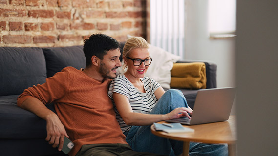 a man and woman sitting on the floor at a table looking at their laptop together