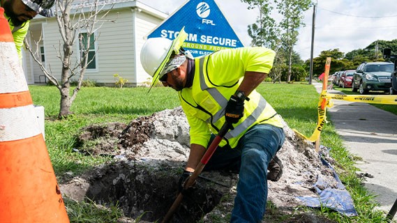 an fpl worker in the field digging a hole for powerline undergrounding