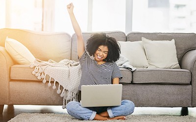 Woman excitedly raising up her arm while looking at computer screen