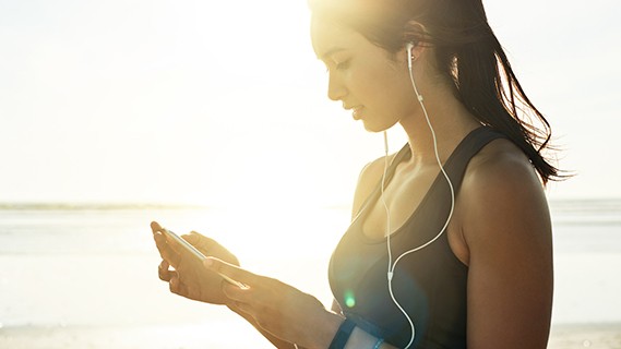 Woman on the beach looking at mobile device with headphones in