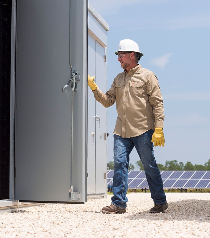 an fpl worker in PPE assessing battery storage at a solar energy center