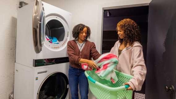 Two African American women putting clothes into a washer
