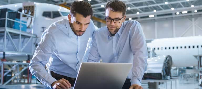 Two men wearing light blue collar shirts looking at a laptop
