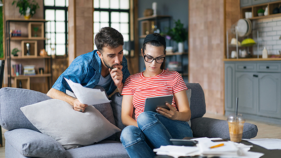 man and woman sitting on couch looking at bill