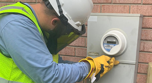 FPL employee working on a meter while wearing a lime green vest, yellow gloves, face shield and white helmet