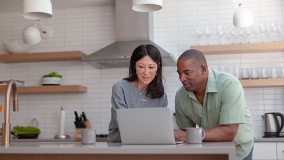 a couple looking at a laptop in their kitchen