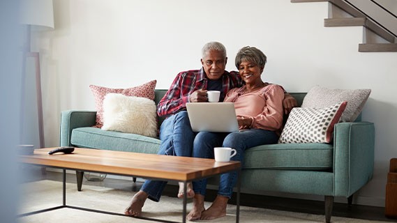 an elderly couple sitting on a couch in a living room using a laptop
